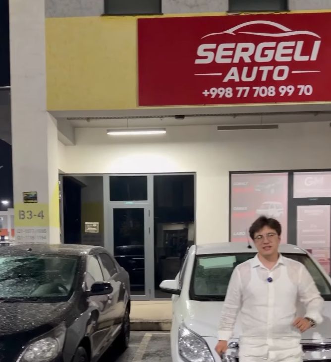 Sergeli Avto salonining tungi fasadi, oldida oq va qora Cobalt